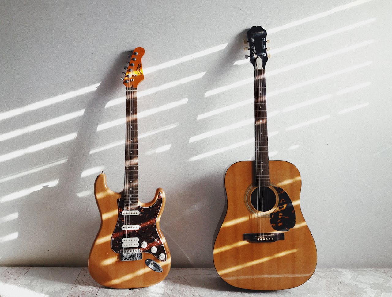 A minimalist scene featuring an acoustic and electric guitar against a white wall, perfect for music enthusiasts.